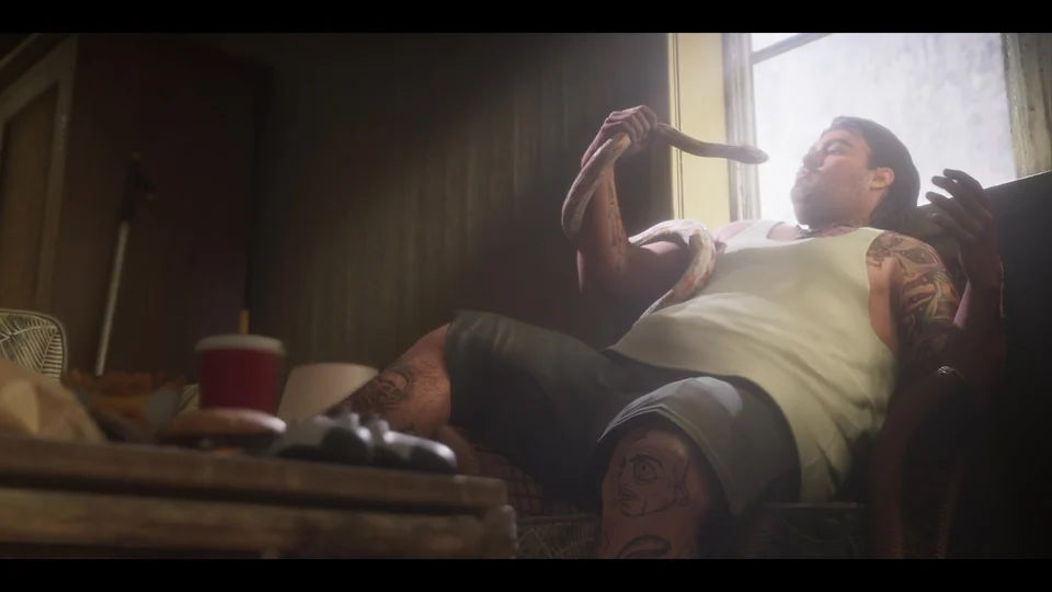 Мужчина, похожий на Кэла Хэмптона, держит змею в кресле; на столике еда и игровой контроллер